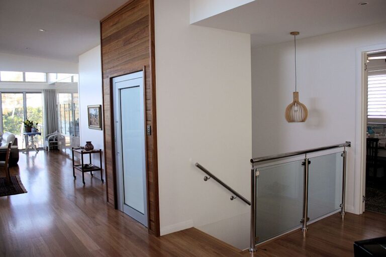 Timber clad lift shaft with a frosted glass door beside the stairwell and an open plan living area