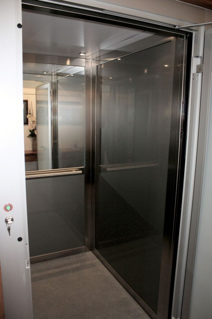 Inside the E1 lift with dark glass walls, brushed stainless steel profiles and a half-height mirror