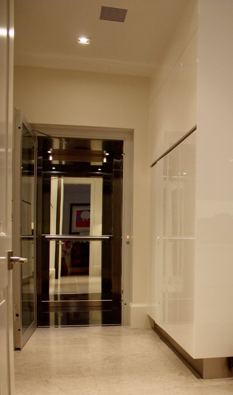 The lift at the end of a corridor with white panelled walls and a stone floor