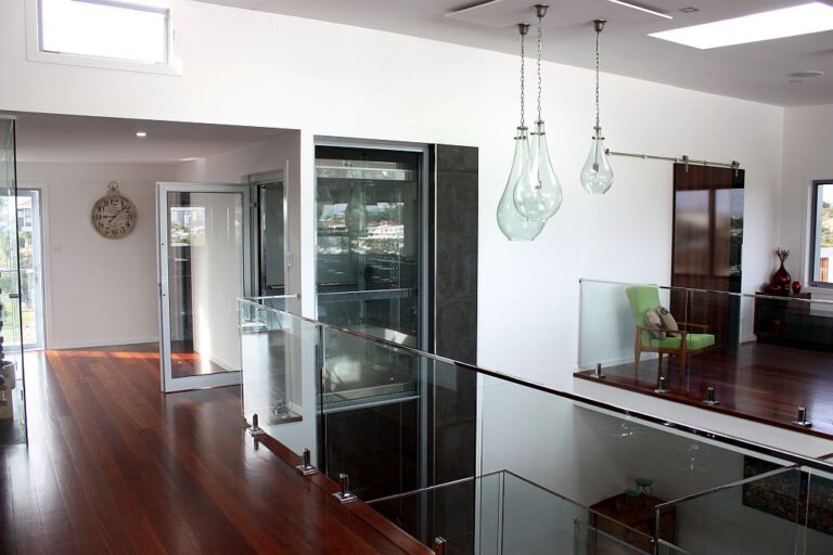 Polished timber floor, glass balustrade and a lift beside glass pendant lights