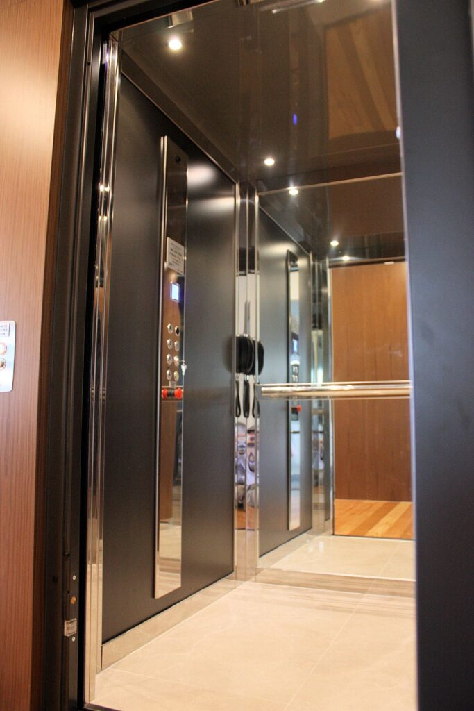 Open lift door revealing a dark cabin with a timber panelled wall and stainless handrail