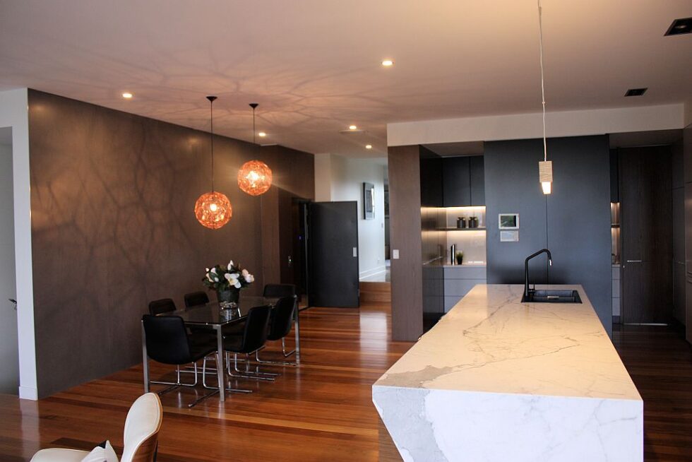 Open plan kitchen and dining area with a marble island and pendant lights, the lift door beyond
