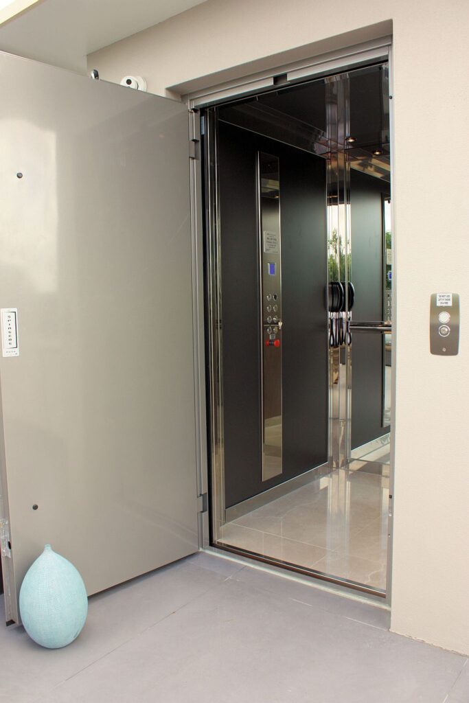 Rooftop lift door opened outward from a pale wall with a stainless cabin inside