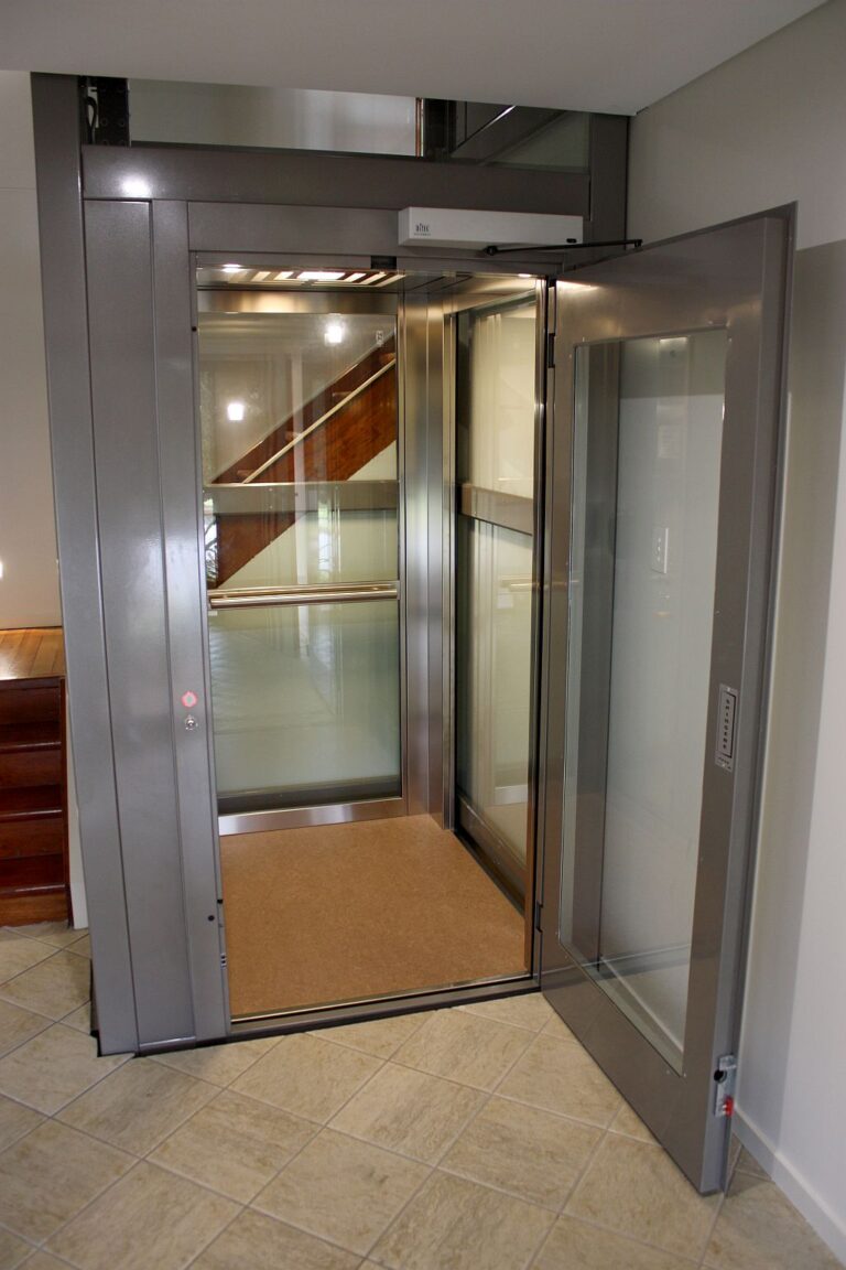 Open ElfoLift door with a grey metal frame and a clear glass side wall on a tiled floor