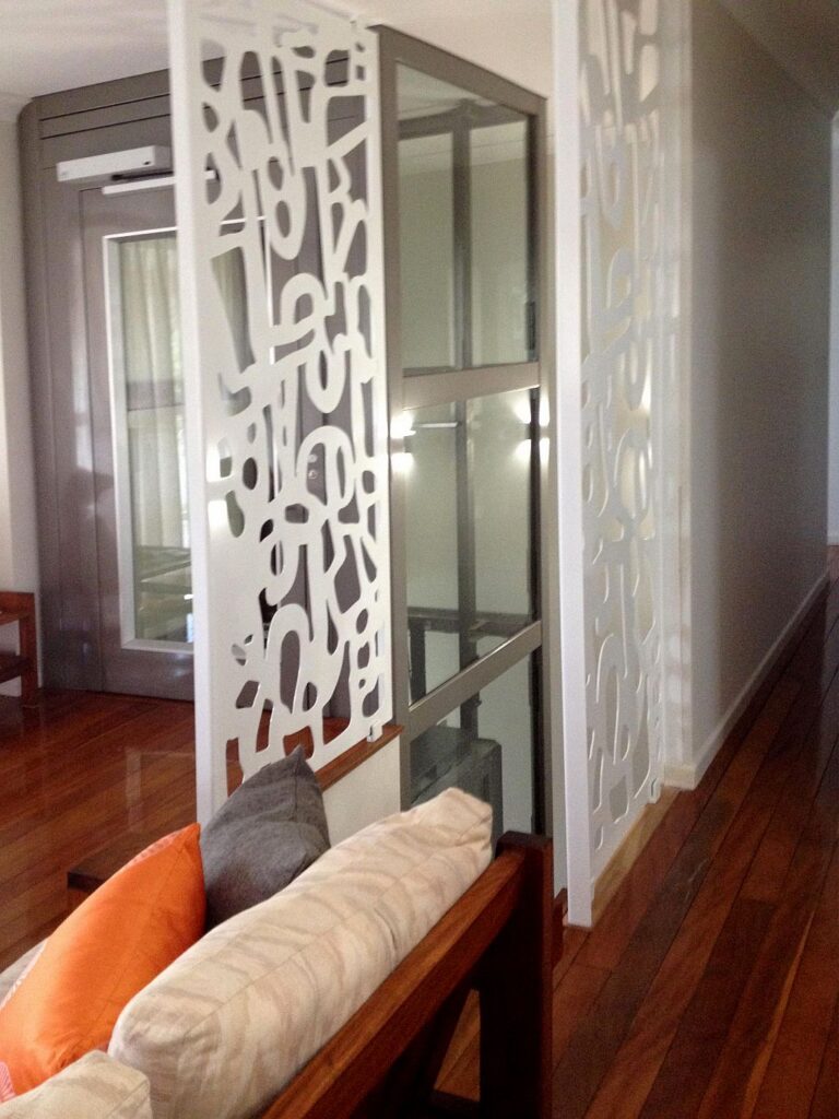 Laser-cut white screen beside the glass shaft and a sofa with orange cushions