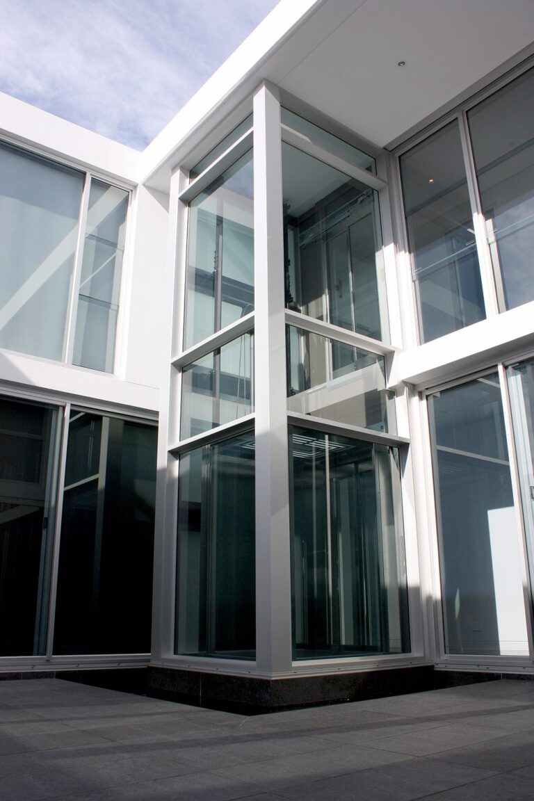 Corner of the glass-walled E2 lift shaft rising above the stone-paved courtyard of a Dover Heights home