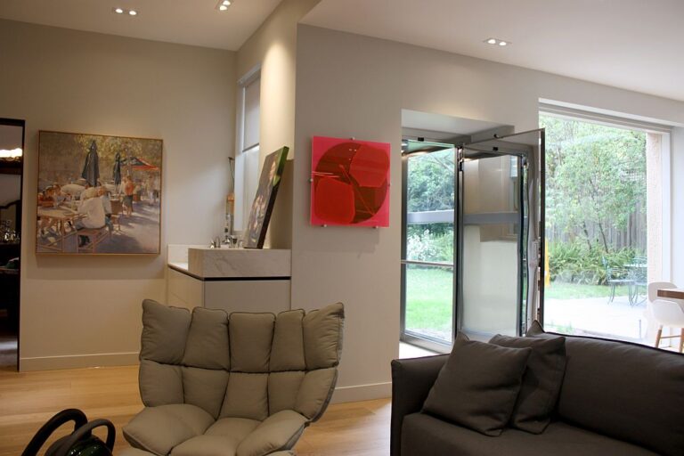 Lounge room with artworks and the open glass lift door beside a large window onto the garden