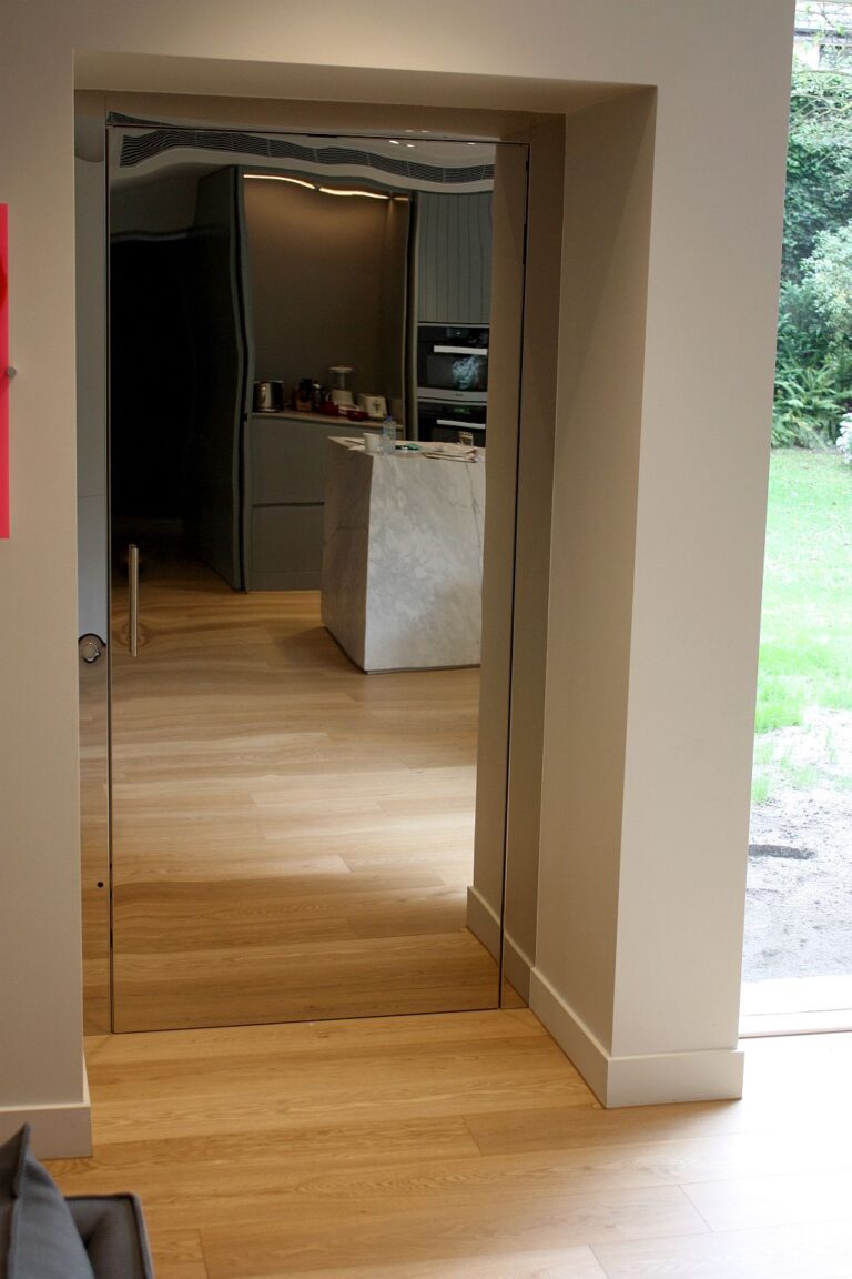 Super polished stainless steel lift door in a doorway opening onto a timber-floored kitchen with a stone island