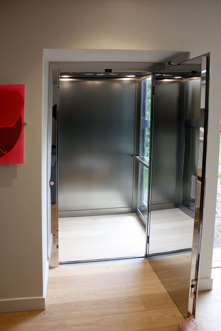 Open E1 lift door showing a brushed stainless steel look car interior on a timber floor