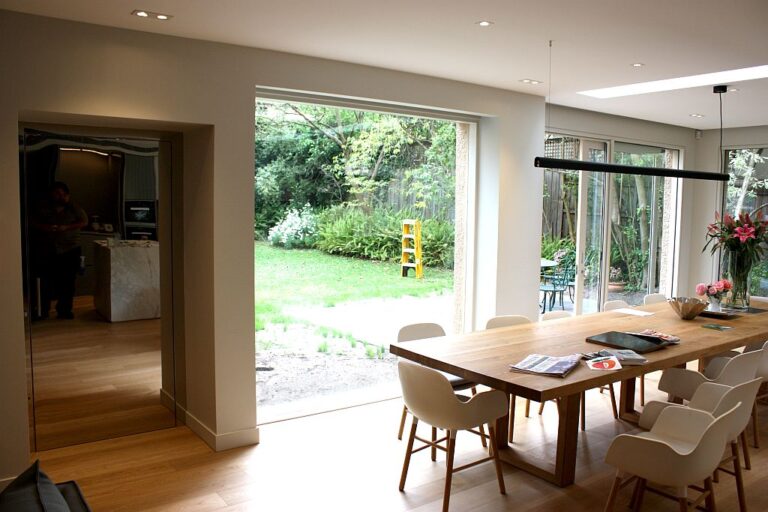 Dining area with a timber table and white chairs opening to a garden