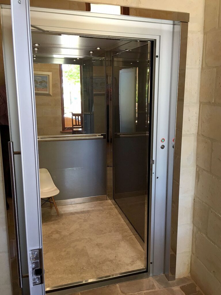 ElfoLift cabin with a mirrored back wall and a white chair seen through the open glass door