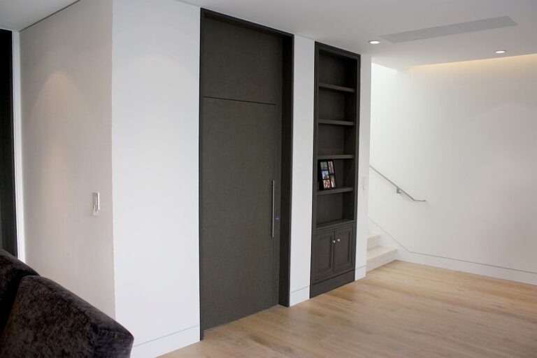 Dark lift door beside built in shelving and a staircase with light timber floor
