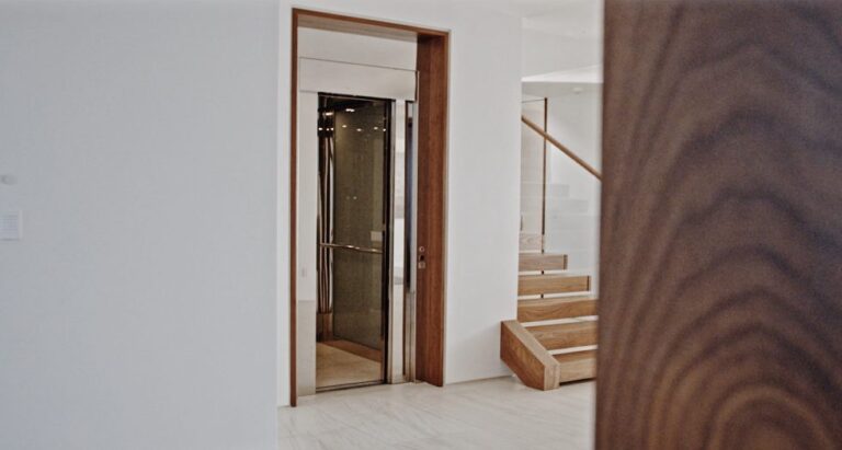 Lift with a timber frame door seen from a white hallway beside a timber panel