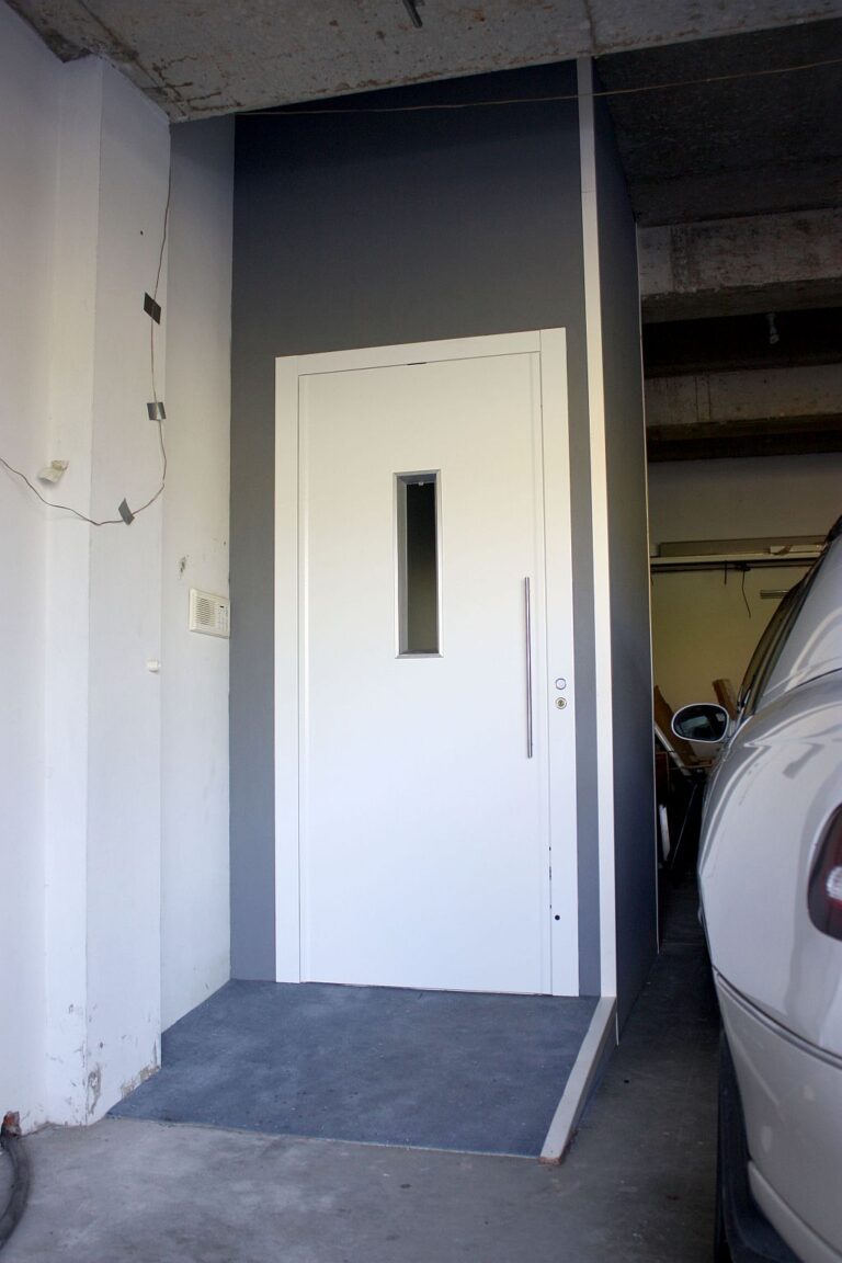 The finished white lift door with a narrow window on the garage level beside a parked car