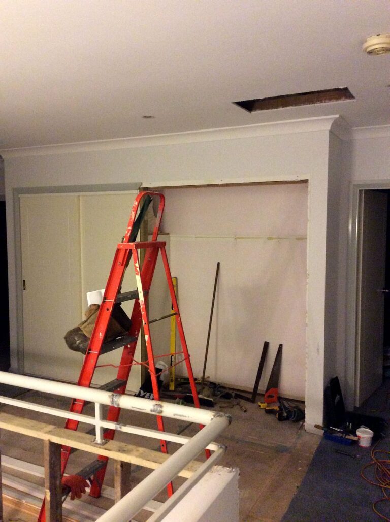The emptied linen cupboard recess with a red step ladder and a small opening cut in the ceiling above