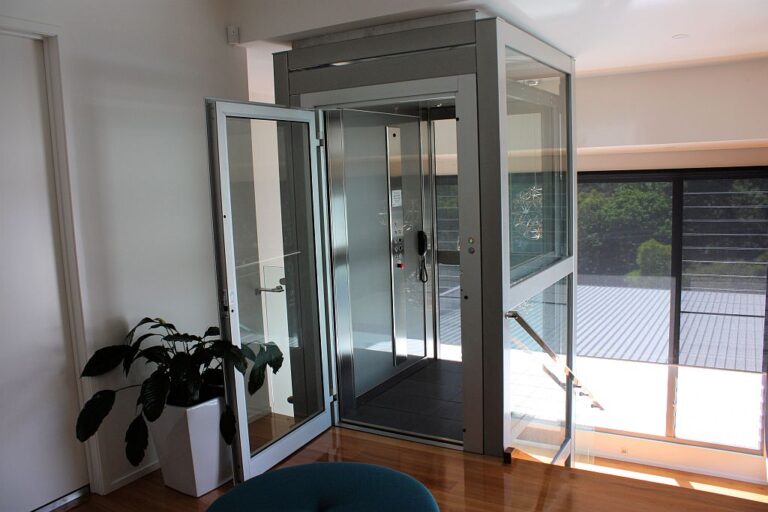 Four-level glass home lift with its landing door open beside a potted plant and a deck view in Ashgrove