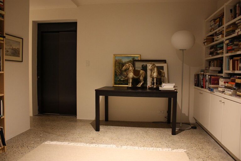 Study with a desk, floor lamp and a dark Inox Nero Satinato lift door in the wall