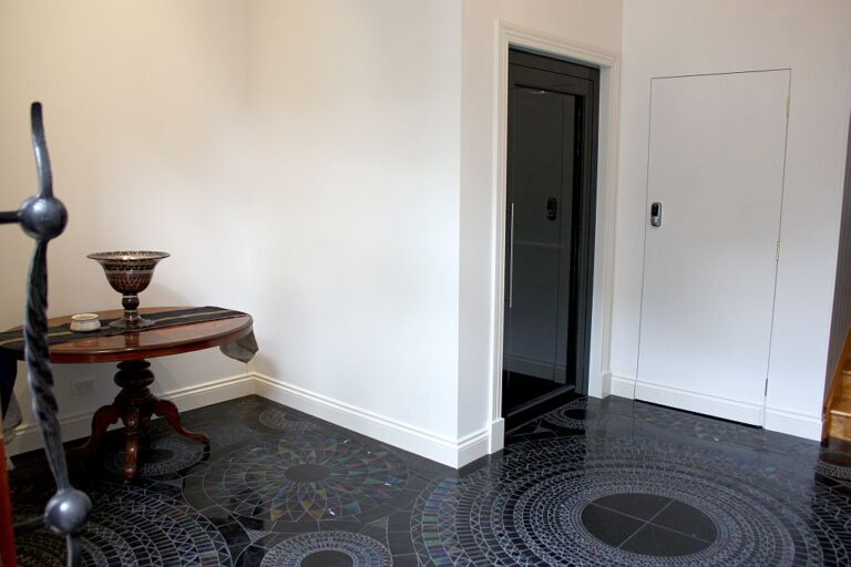 Dark lift door in a white hallway wall above a black mosaic tile floor in the foyer