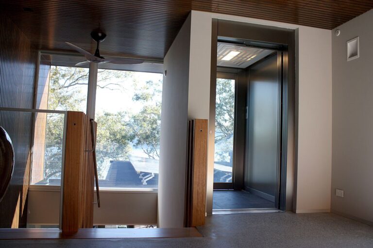 Lift door on the upper landing beside a large window with treetop views, Northern Beaches home