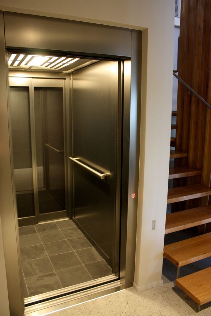 Lift cabin with dark metal walls, slate floor and a stainless handrail beside timber stairs