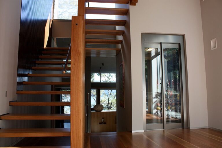 Timber open-tread staircase beside a home lift with a glass door in a Northern Beaches home