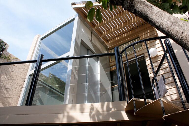 Glass lift shaft beside a timber pergola and black railing seen from below in Sandringham