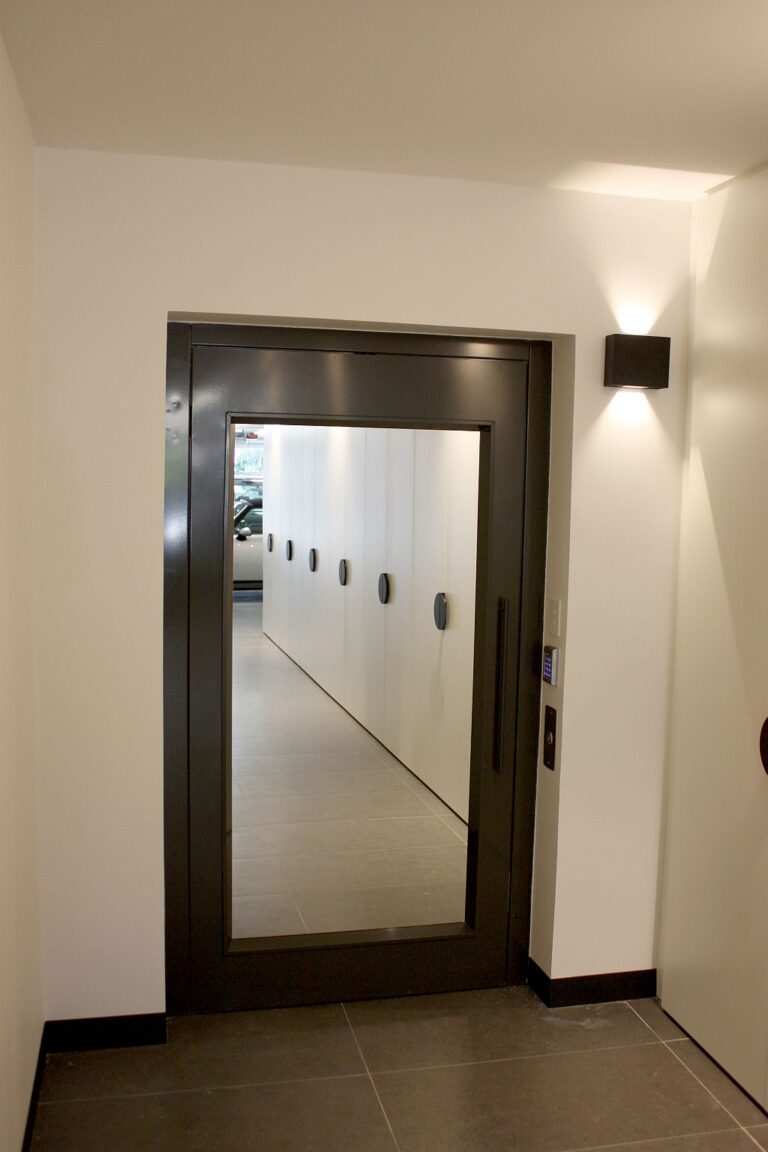 Black framed lift door with a mirrored glass panel beside a wall light at the garage level