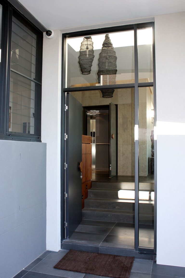 Entry doorway with glass panels and hanging lights, seen from outside the house, with the lift door visible inside
