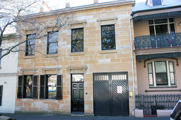 Sandstone fronted heritage townhouse with black timber carriageway doors in Sydney