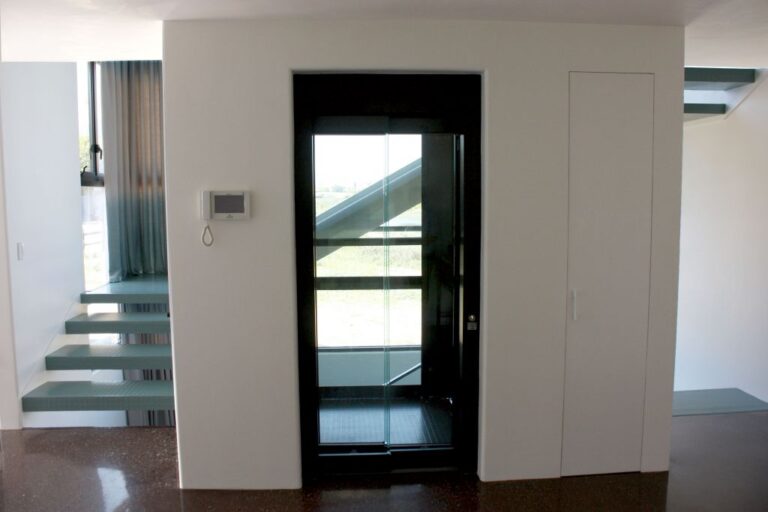 Black-framed glass Lift Shop home lift with sliding door beside a floating glass-tread staircase