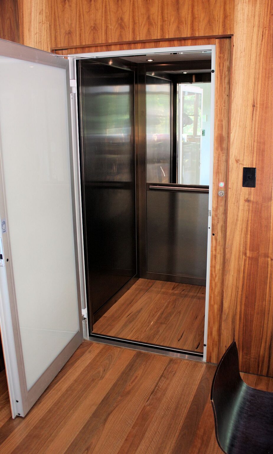 Open ElfoLift door with milk white glass, showing the Bronzo stainless steel cabin with half mirror, handrail and timber floor