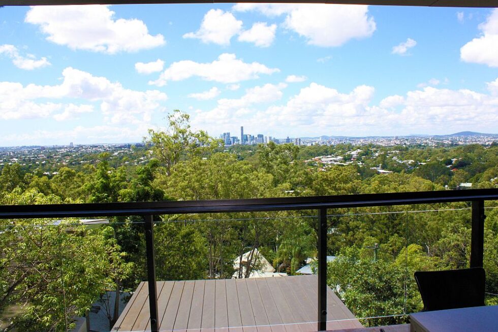 View over treetops to the Brisbane city skyline from a deck with a black balustrade at the hilltop home