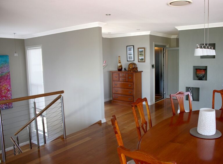 Dining room with a timber table, a wire stair rail and a lift door at the back in Shelly Beach