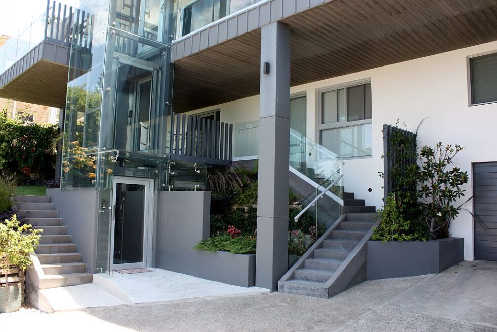 The lower entry of the glass lift shaft with a frameless glass awning above the door