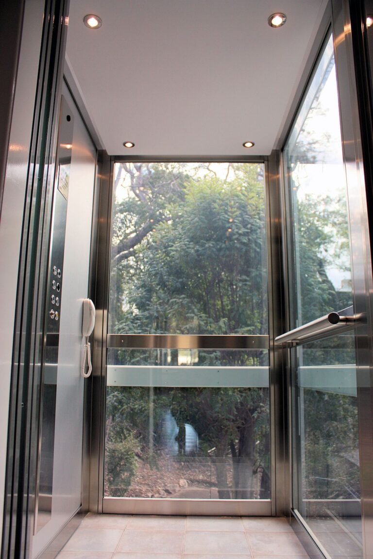 Lift cabin wall with a brushed stainless steel control panel, phone and glass side walls