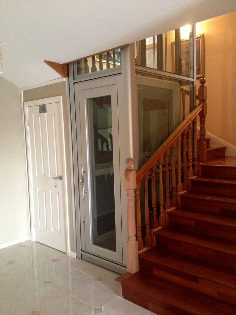 Finished glass lift at the foot of a timber staircase beside a white door