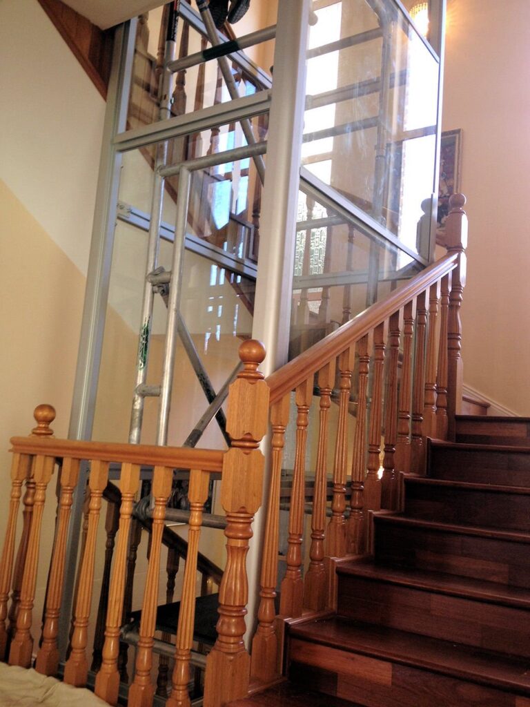 Timber stair balustrade in front of a tall glass lift shaft with a metal frame