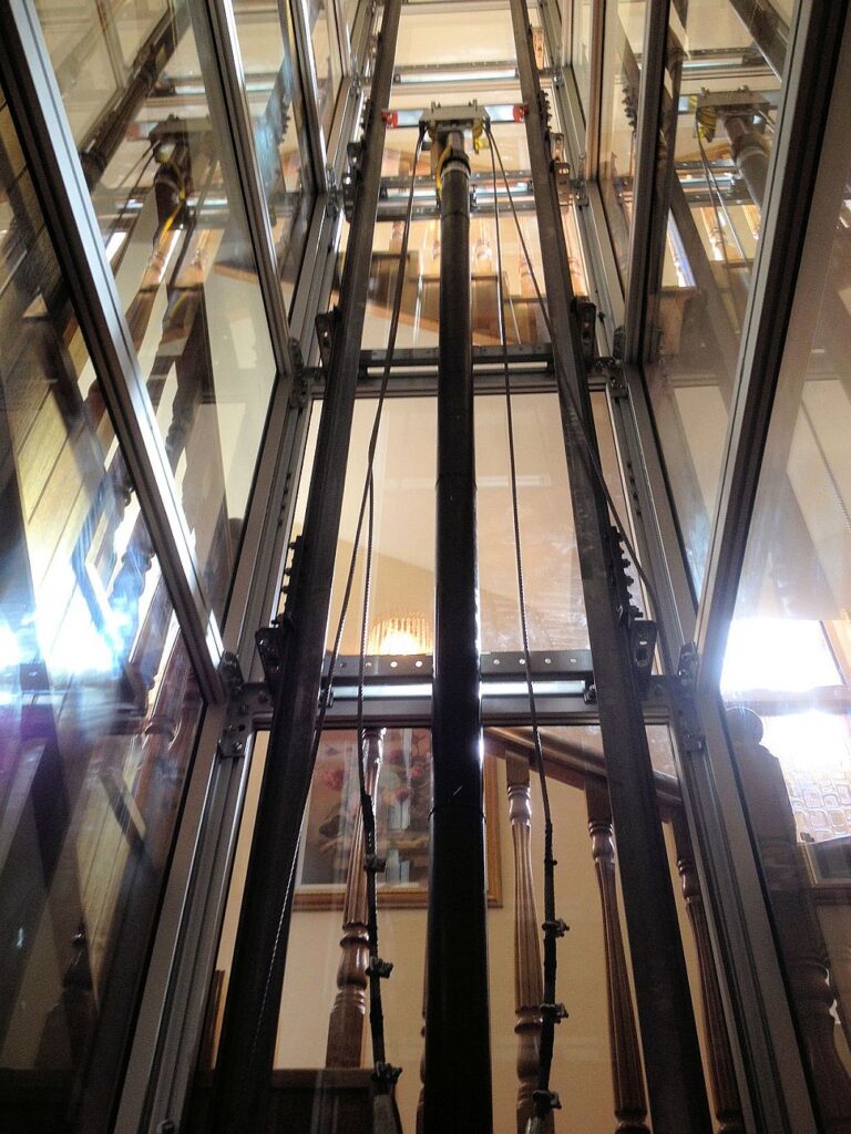 Looking up inside a glass lift shaft with guide rails and cables