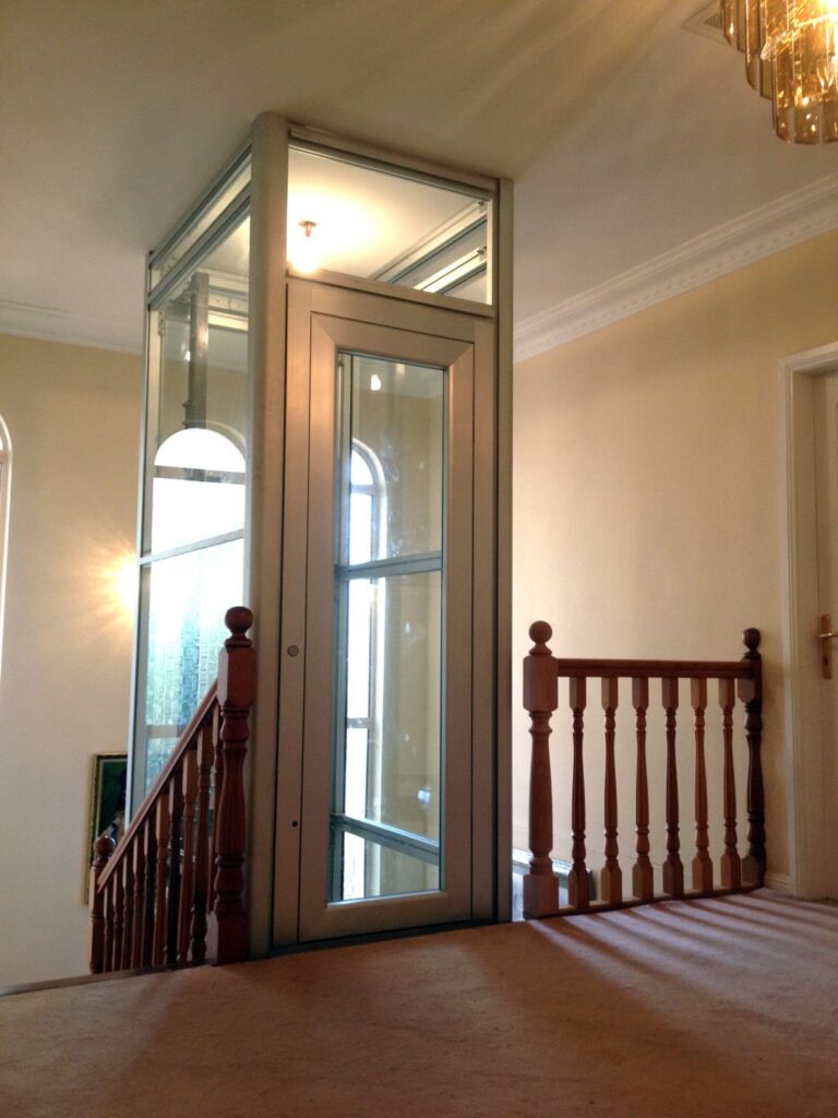 Glass lift on an upstairs landing beside a timber balustrade and arched window