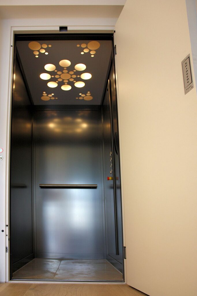 Open E1 lift door showing a dark brushed skinplate cabin with a decorative lit ceiling in a Brighton townhouse