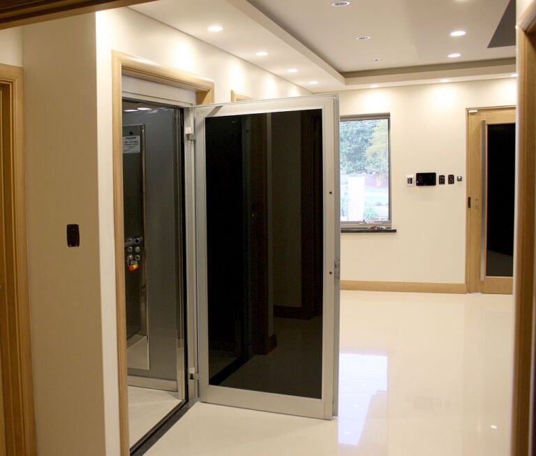 Open lift door with black glass and an aluminium frame beside timber trim