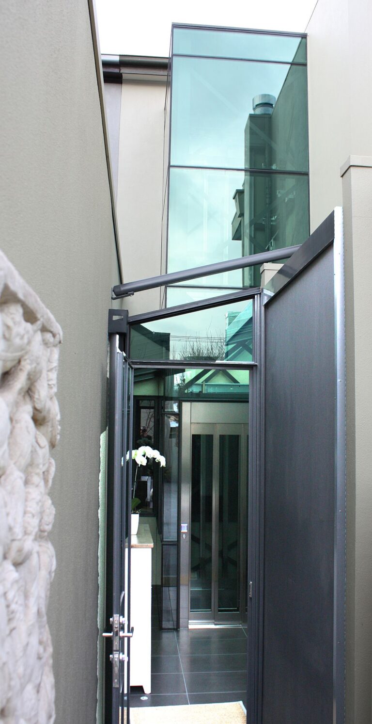 The glass lift shaft rising in the rear alcove beside the side passage of the Albert Park terrace
