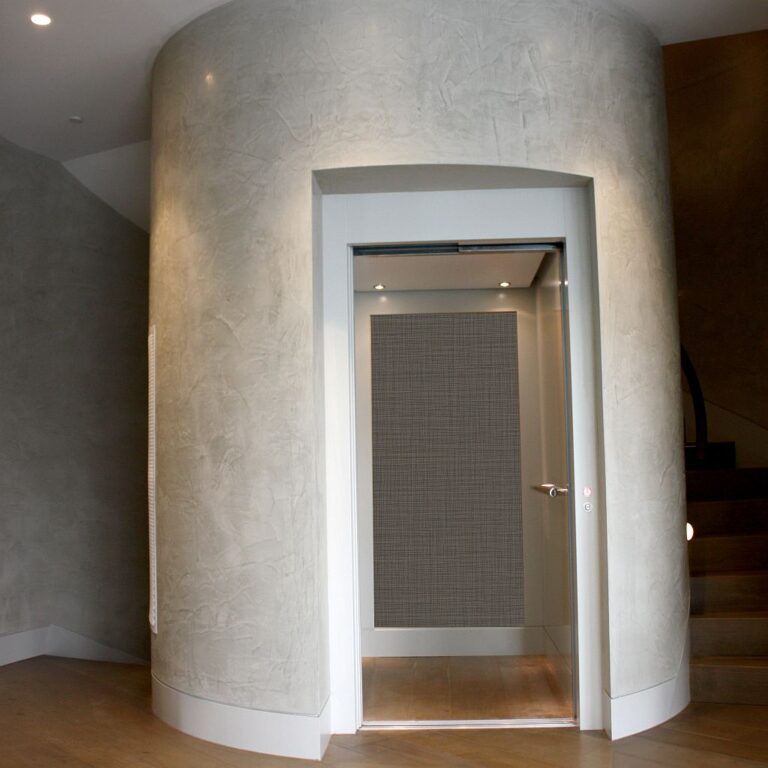 Lift door with a woven panel set in a curved rendered wall beside stairs