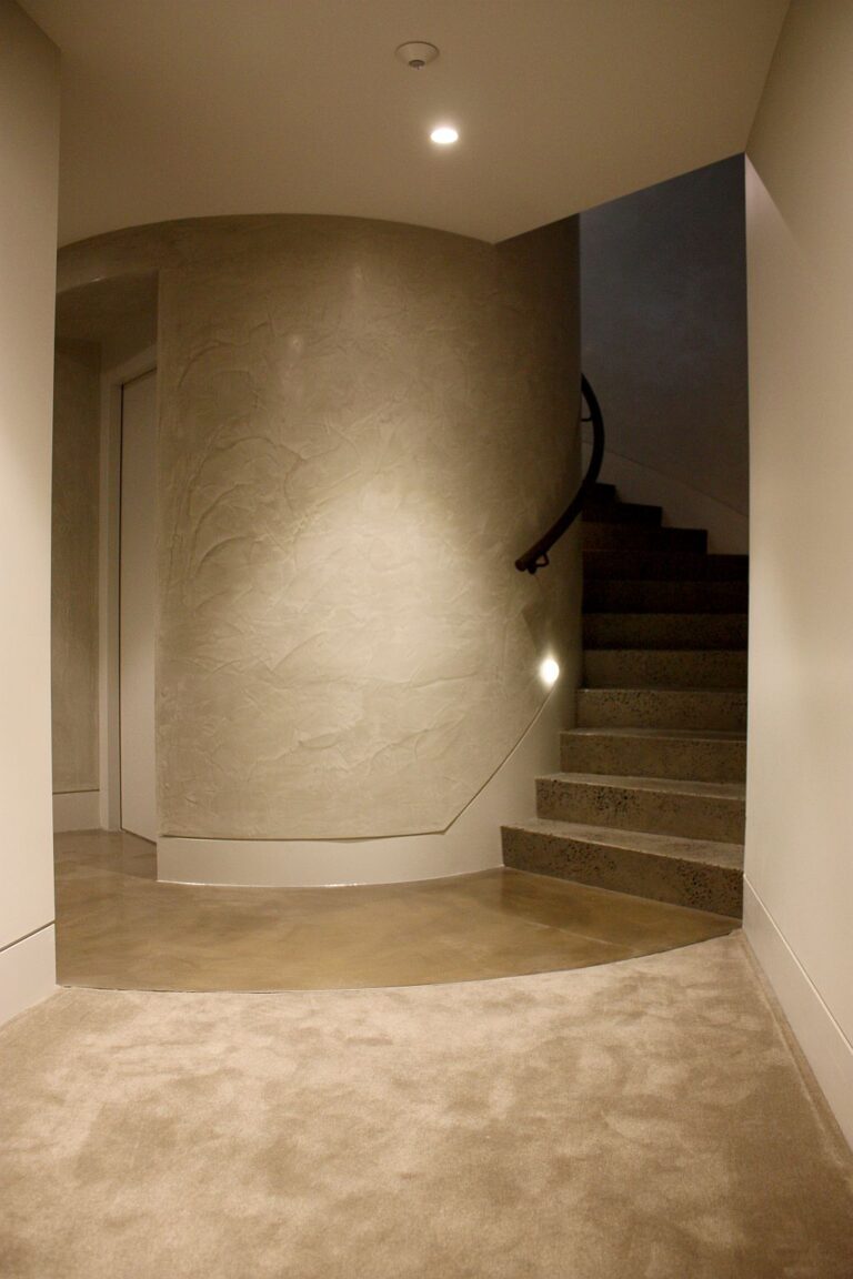 Curved textured shaft wall beside a stair with a handrail and a carpeted landing