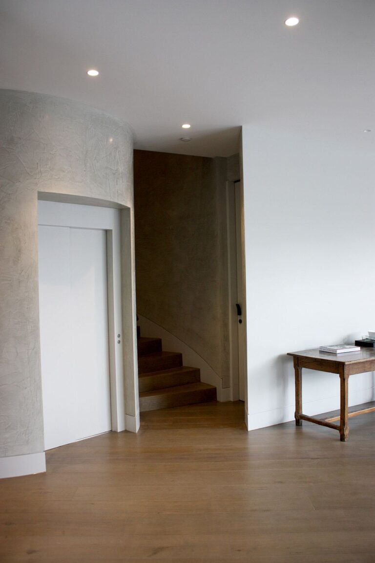 Lift door in the curved shaft beside a timber staircase and console table