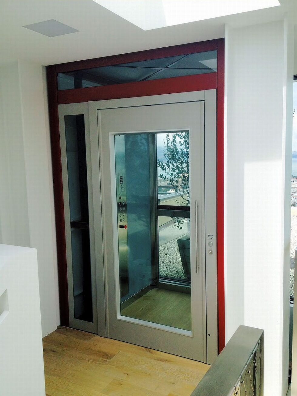 Finished glass lift landing door with a red frame and clear glass panel, opening onto a timber floor in the San Francisco home