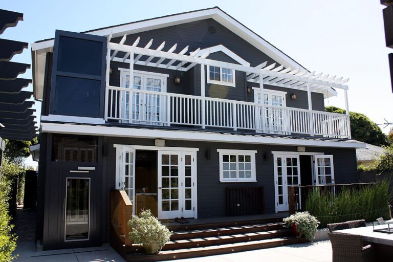 Dark grey two-storey home with white balcony railings and a pergola, the lift shaft at the left