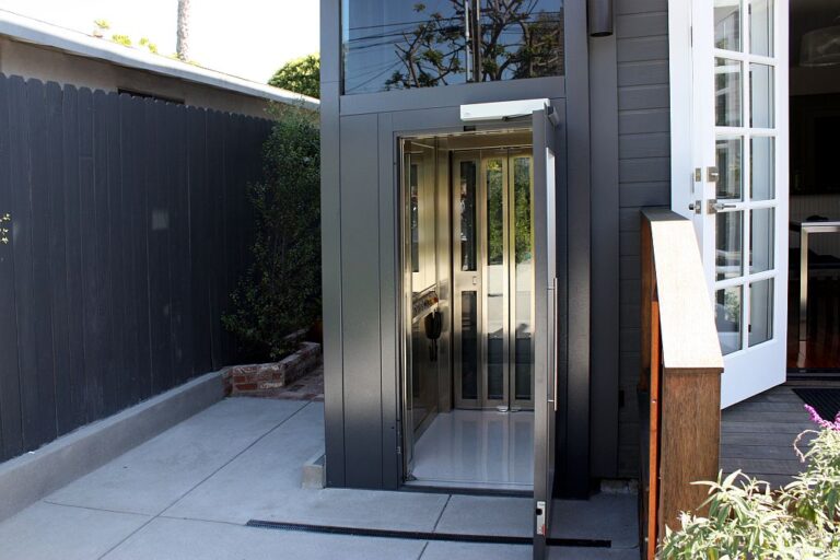 Outdoor lift entry with an open glass door beside a dark fence and the courtyard