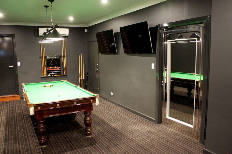 Mirrored stainless steel lift door in a dark games room with a billiards table