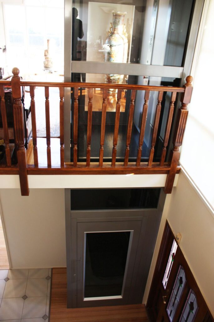 Timber balustrade at the upper landing with the glass-shaft lift and its lower door behind